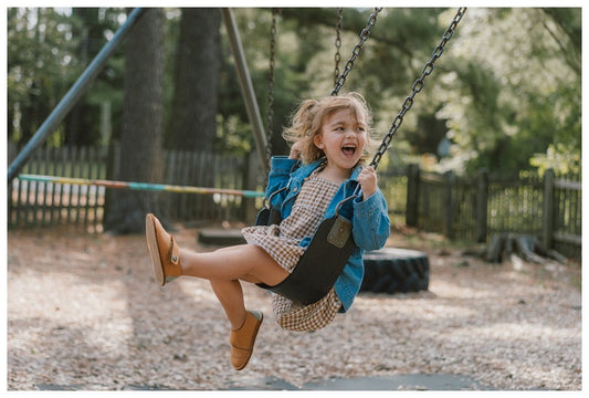Toddler on a playground swing wearing closed-toe barefoot shoes with a wide toe box