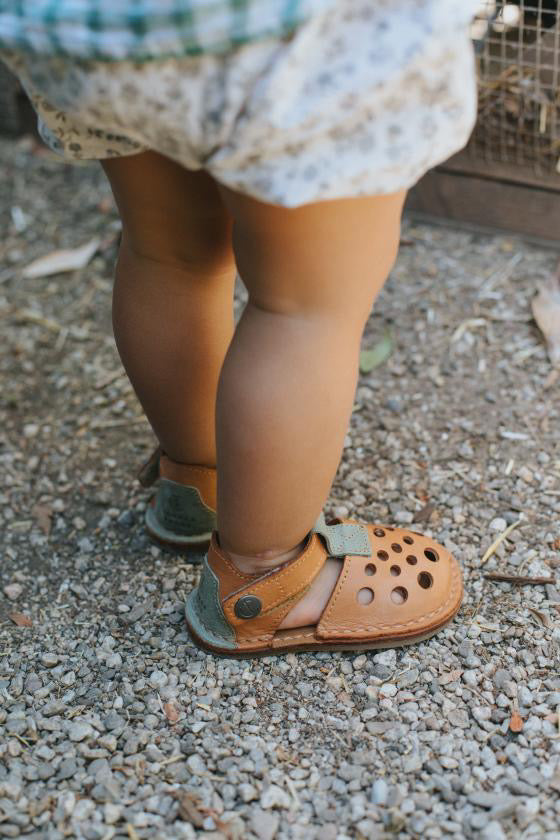 Green barefoot sandals worn by child walking on gravel