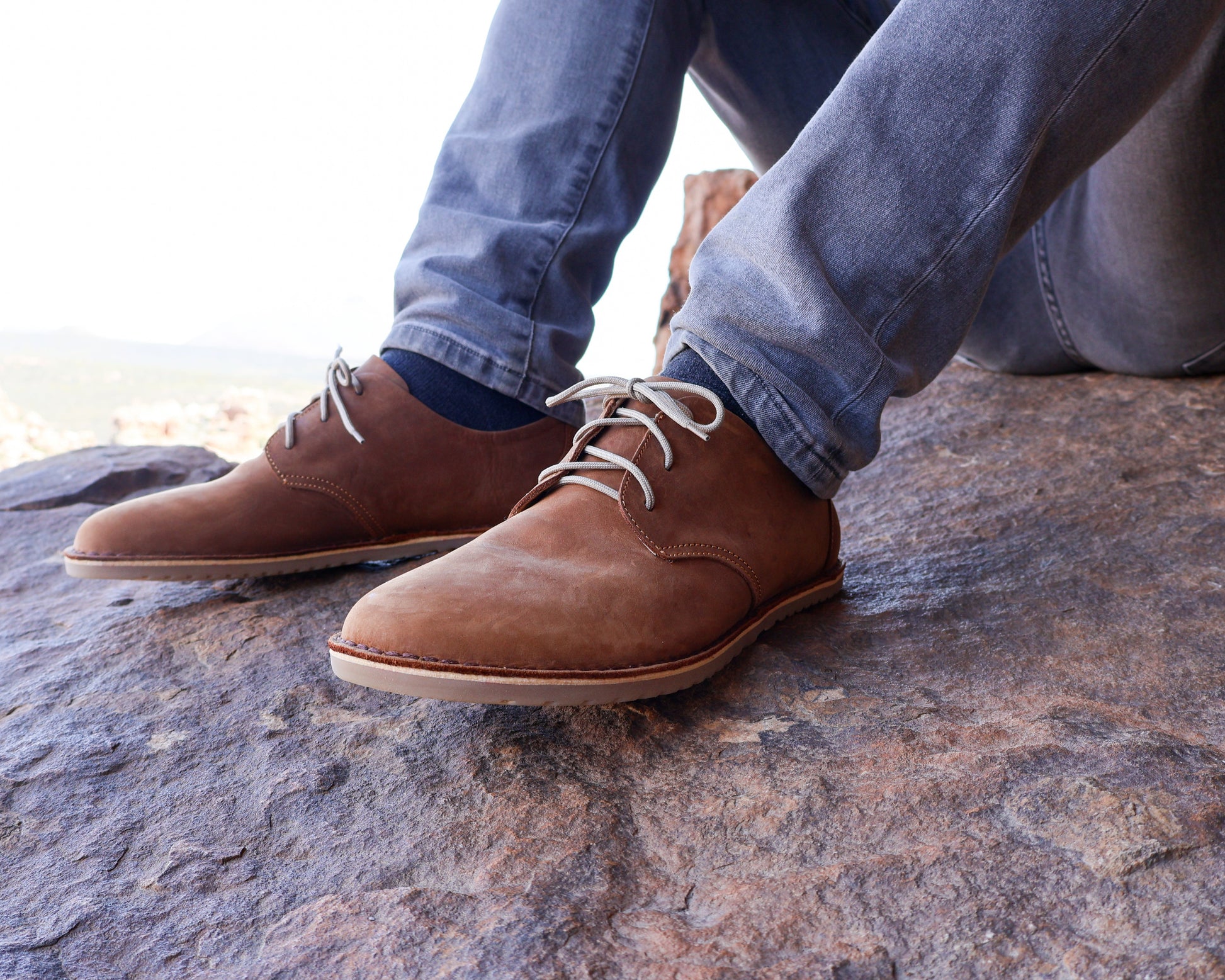 Man wearing Common Tread Traversa men’s barefoot leather shoes while seated outdoors on rocks