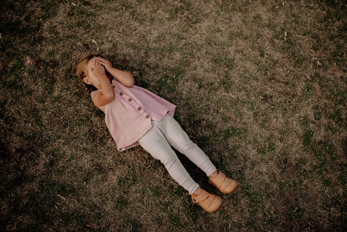 Child lying on grass wearing Common Tread Evergreen shoes in a relaxed outdoor setting